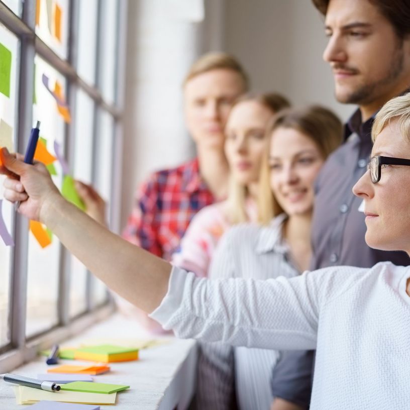 Frau befestigt mit Gruppe Notizzettel an Wand 