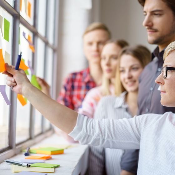 Frau befestigt mit Gruppe Notizzettel an Wand 