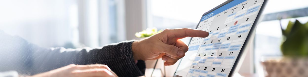 Eine Person zeigt mit dem Finger auf einen Kalender auf dem Laptop